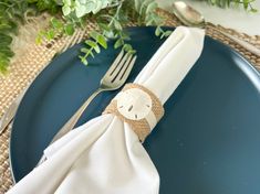 a blue plate topped with a white napkin and silverware next to a green plant