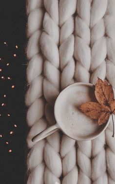 a white bowl with a brown leaf on top of it next to a knitted blanket