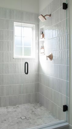 a white tiled bathroom with a glass shower door and black handles on the faucet