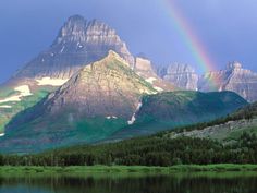 a rainbow shines in the sky over a mountain range with a lake below it