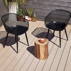 three black chairs sitting on top of a wooden floor next to a tree stump and potted plant