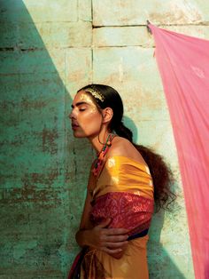 a woman standing in front of a wall with her head turned to the side, wearing a yellow and red sari