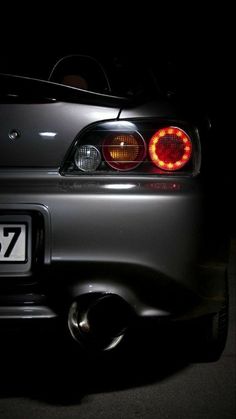 the back end of a silver sports car with its tail lights turned on at night