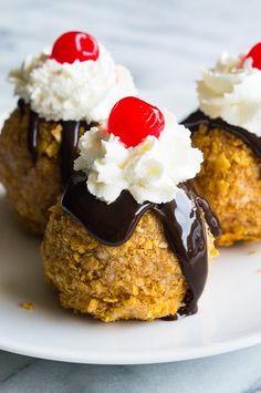 three desserts on a white plate with chocolate sauce and whipped cream, topped with cherries