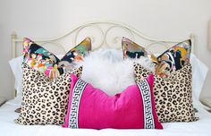 three pillows on top of a white bed with pink and leopard print pillowcases