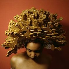 a man with an elaborate head piece on top of his head, against a red wall