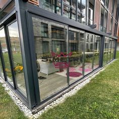 an outside view of a building with glass walls and furniture on the grass in front of it