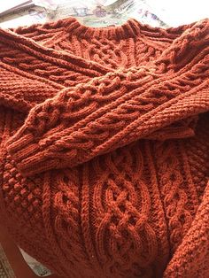 an orange knitted sweater sitting on top of a wooden chair next to a window