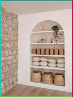 a shelf with baskets and towels on it next to a stone wall in a room