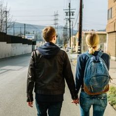 a man and woman walking down the street with a backpack on their back, holding hands