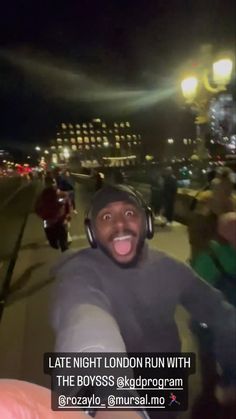 a man with headphones on taking a selfie in front of some people at night