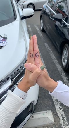 two people holding hands with small tattoos on their fingers, in front of parked cars