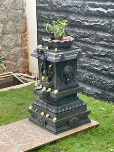 there is a statue in the grass with flowers growing out of it and a potted plant on top