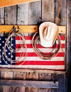 a cowboy hat, lasso and american flag hanging on a wooden wall