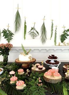 a table topped with cakes and cupcakes covered in frosting surrounded by greenery