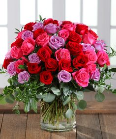 a vase filled with red, pink and purple roses on top of a wooden table