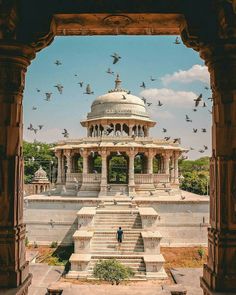 birds are flying in the air over a building with a dome on top and stairs leading up to it