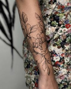 a woman's arm with flowers and leaves on the forearm, in black ink