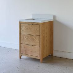 a wooden cabinet with two drawers and a white counter top, against a white wall