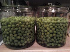 two glass jars filled with green beans sitting on top of a wooden counter next to each other