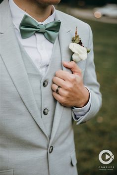 a man wearing a gray suit and green bow tie holding a white rose in his lapel