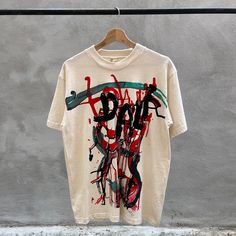 a white t - shirt with red, black and green spray paint on it hanging from a clothes line