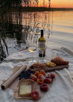 a wine glass and some food on a towel near the water at sunset or sunrise