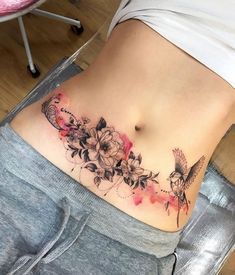 a woman's stomach with flowers and a humming tattoo on her side ribcage