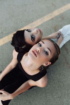 two beautiful young women standing next to each other on the street together, looking up at the camera