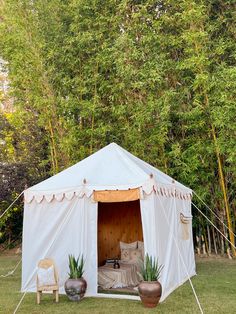 a white tent set up in the middle of a field with two chairs and potted plants