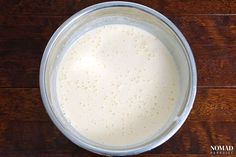 a glass bowl filled with white liquid on top of a wooden table next to a knife