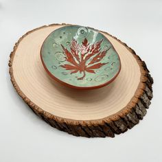 a green bowl with a red leaf on it sitting on top of a tree stump