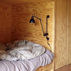 an unmade bed in a room with wood paneling and a lamp on the wall