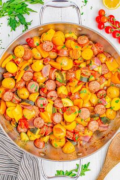 a pan filled with sausage and tomatoes on top of a white table next to fresh herbs