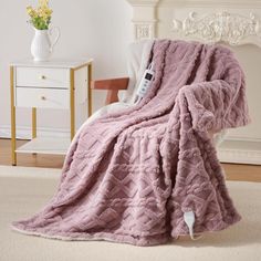 a pink blanket sitting on top of a chair next to a white dresser and fireplace