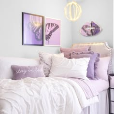 a white bed topped with lots of pillows next to two framed pictures on the wall