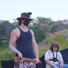 a man wearing a mask while holding a skateboard next to another person sitting down