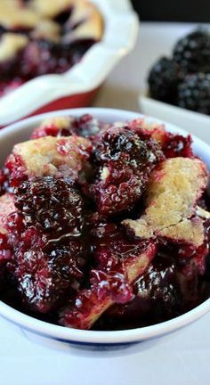 blueberry cobbler in a white bowl on a table with blackberries and other desserts