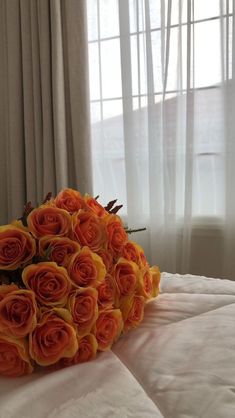 a bouquet of orange roses sitting on top of a white bed in front of a window