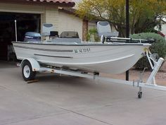 a white boat parked in front of a house with a trailer attached to the side