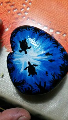 a hand holding a blue and black painted rock with an image of a turtle on it