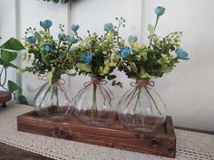 three glass vases with flowers in them on a wooden shelf next to a wreath