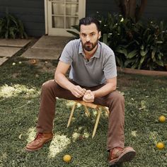 a man is sitting on a chair in the grass with some oranges around him