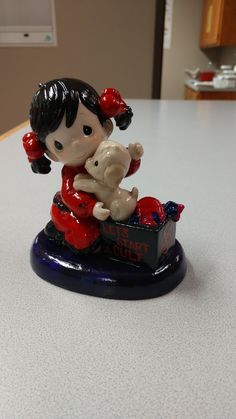 a small figurine of a girl holding a teddy bear on top of a table