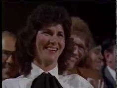 a woman wearing a white shirt and black tie with other people in the background smiling