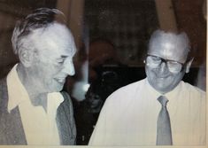 two men in suits and ties standing next to each other with their faces close together