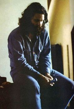 a man with long hair sitting on top of a bed holding a remote control in his hand