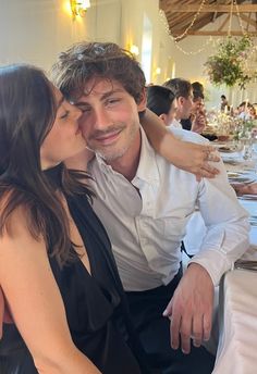 a man and woman kissing each other at a dinner table with people in the background