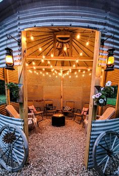 an outdoor seating area with chairs and lights on the roof, surrounded by metal barrels