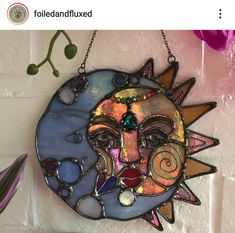 a sun face hanging on a wall with beads and other things around it, including flowers